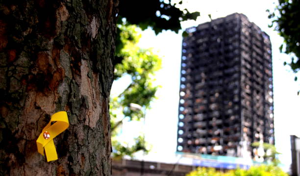 Grenfell-Turm im Hintergrund mit einem gelben Band, das an die Verlorenen erinnert und an einen Baum geheftet ist